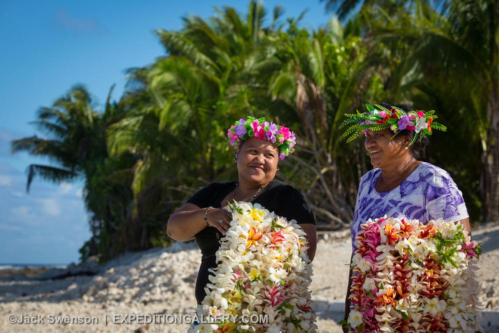 This image: Local women with arms full of flower leis to welcome visitors to Manihiki Atoll in the northern Cook Islands.